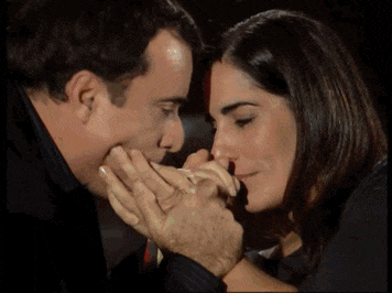 a man kisses a woman 's hand while they are looking into each other 's eyes