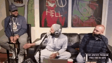 three men are sitting on a couch in front of a sign that says " new hell "