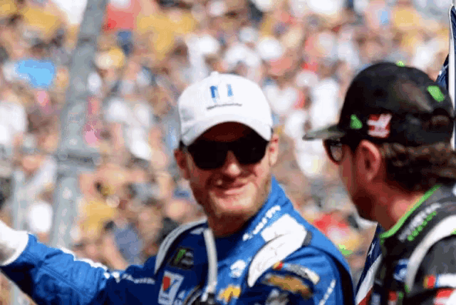 a man wearing sunglasses and a hat with a smiley face on it is talking to another man