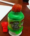 a green bottle with a red straw on top of it is on a wooden table .