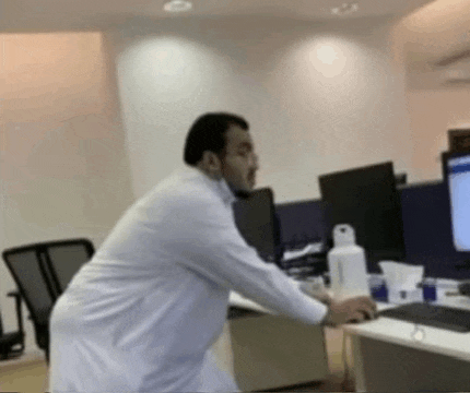 a man in a white robe is standing in front of a desk in an office .