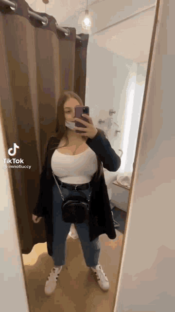 a woman is taking a selfie in a dressing room while wearing a mask .