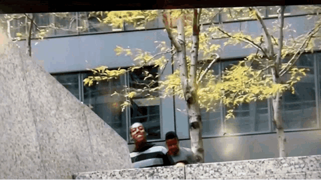two men are standing next to a tree in front of a building ..