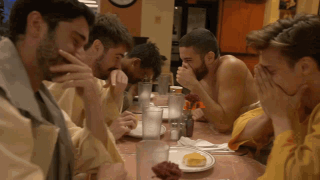 a group of men sit at a table with plates of food and glasses of water