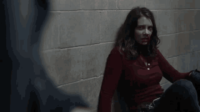 a woman with blood on her face is sitting next to a wall .