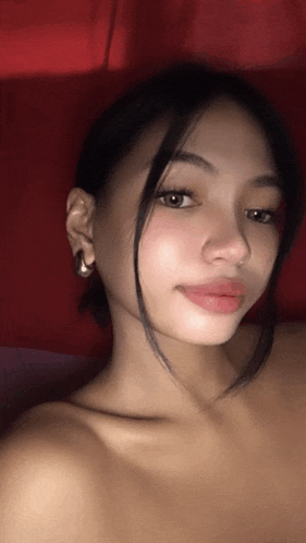 a young woman without a shirt is taking a selfie with a red background