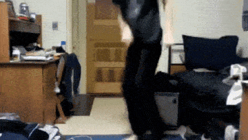 a person is jumping in the air in a room with a desk and a bed