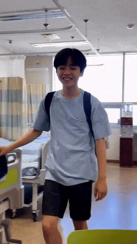 a young man wearing a blue shirt and black shorts is standing in a hospital room