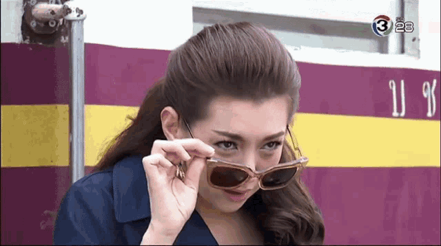a woman wearing sunglasses is standing in front of a purple and yellow wall with the number 3 on it