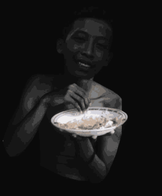a shirtless man is holding a plate of food and smiling .