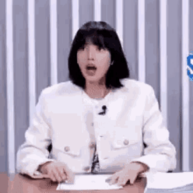 a woman in a white jacket is sitting at a table with her mouth open and a microphone .