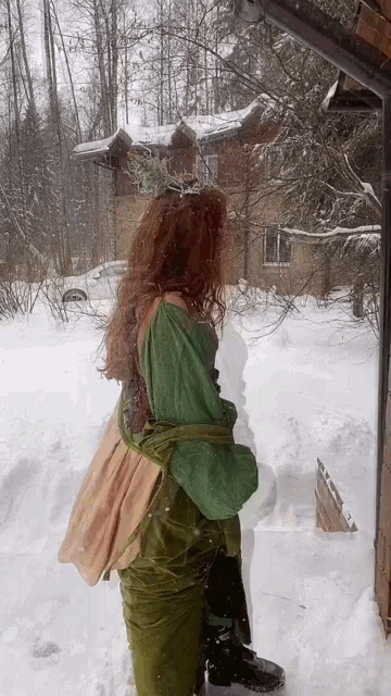 a woman in a green dress is standing in the snow next to a house