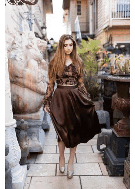 a woman wearing a brown skirt and a lace top stands on a sidewalk
