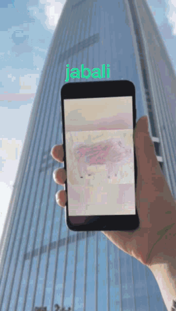 a person is holding a cell phone in front of a tall building that says jabali