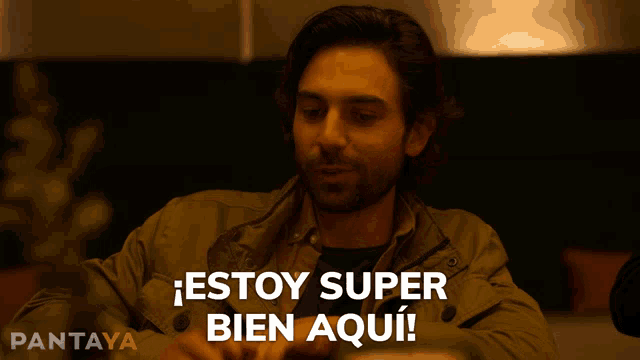 a man sitting at a table with the words estoy super bien aqui written in white