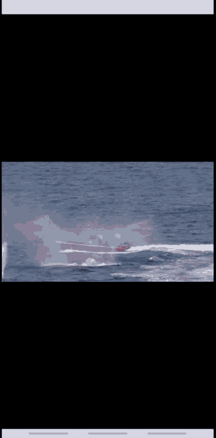 a red boat is floating in the ocean with smoke coming out of it