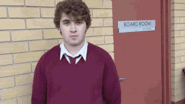 a man in a maroon sweater stands in front of a board room door