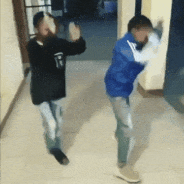 two young men are dancing in a hallway with one wearing a black shirt with the letter r on it