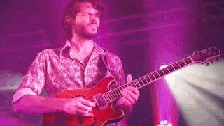 a man with a beard is playing a red guitar in front of a purple background