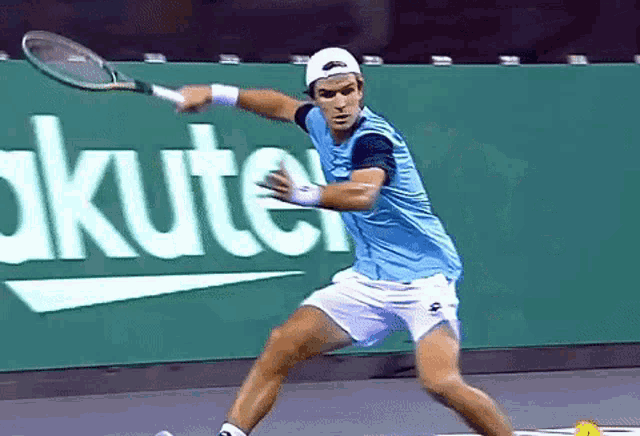 a man in a blue shirt is swinging a tennis racquet in front of an akuter sign