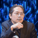 a man wearing glasses and a suit is sitting with his hand on his chin .