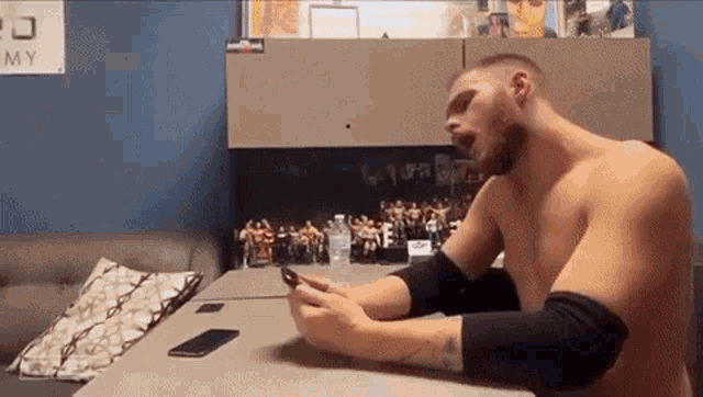 a shirtless man sits at a desk with a sign that says army in the background
