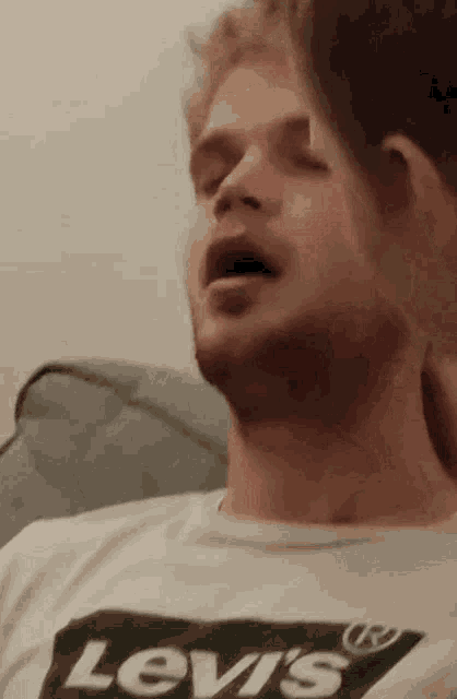 a man wearing a levi 's shirt is laying on a couch with his eyes closed