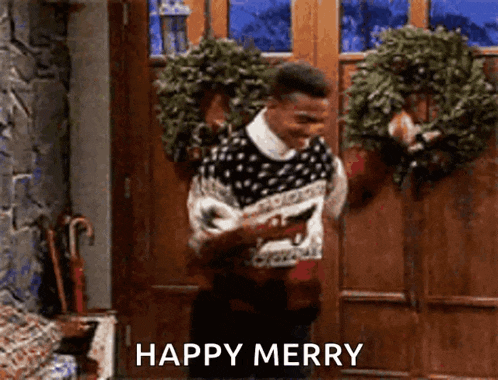 a man in a sweater is standing in front of a door holding a wreath and a phone .
