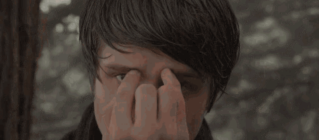 a young man wipes his eyes with his hands
