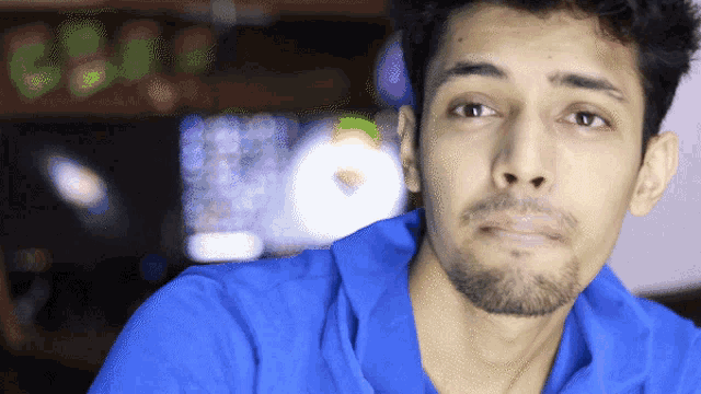 a man in a blue shirt looks at the camera with a clock in the background that reads 6:41