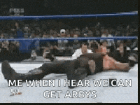 a wrestler is laying on the ground in a wrestling ring while a crowd watches .