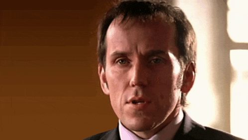 a man in a suit and pink tie looks at the camera with his mouth open