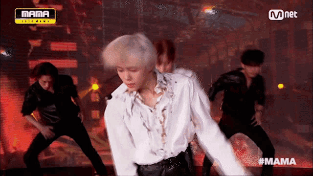 a man in a white shirt is dancing on a stage in front of a mnet sign