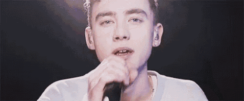 a young man is singing into a microphone on a stage in a dark room .