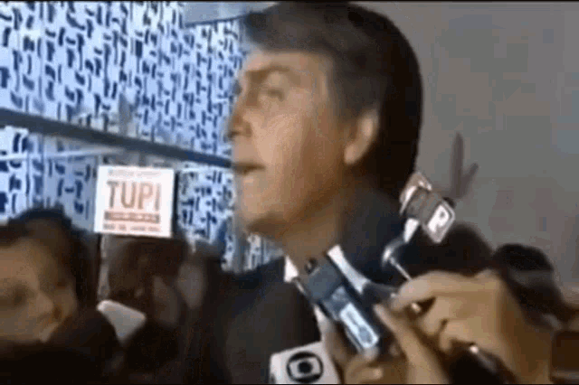 a man is talking into a microphone in front of a sign that says tupi