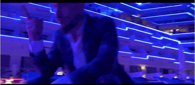 a man in a suit and tie is holding a microphone in a dark room with neon lights .