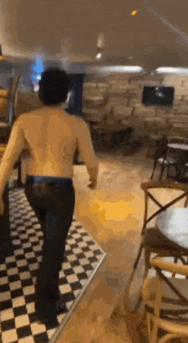 a shirtless man is walking through a restaurant with a checkered floor .