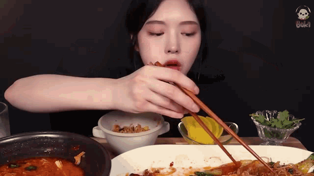 a woman is eating food with chopsticks and a bowl of food in the background .