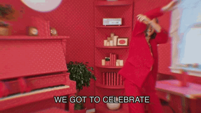 a woman in a red suit is dancing in a red room with the words we got to celebrate