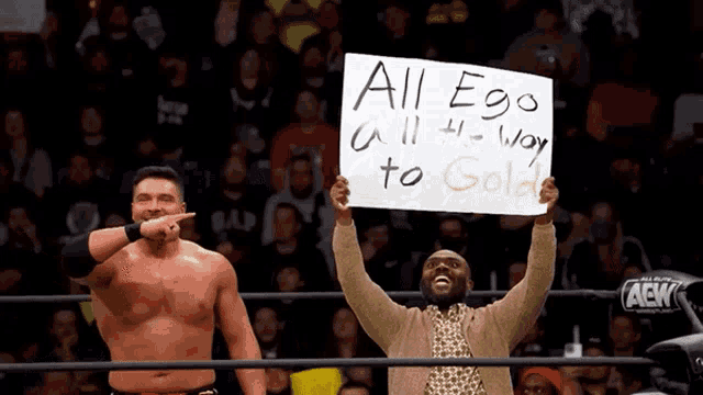 a man in a wrestling ring holds a sign that says all ego all way to gold