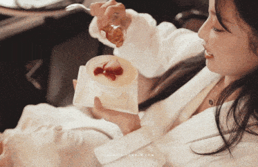 a woman in a bathrobe is eating a dessert with strawberries and honey