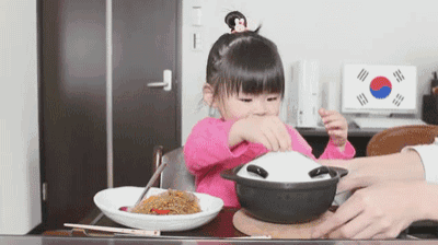 a little girl sitting at a table with a bowl of food