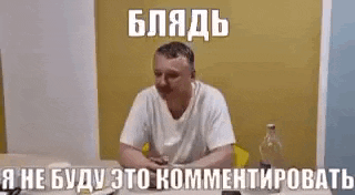 a man is sitting at a table with a bottle of alcohol in front of him and making a funny face .