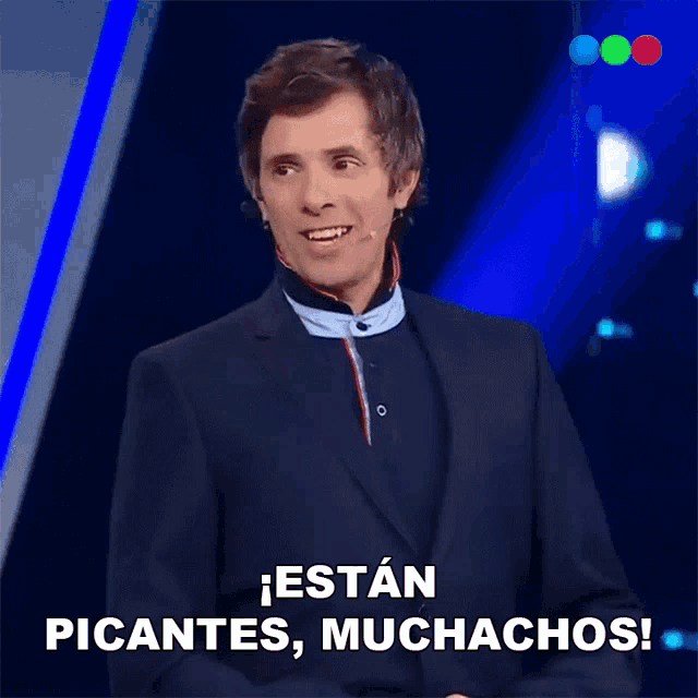 a man in a suit stands in front of a microphone and says estan picantes muchachos