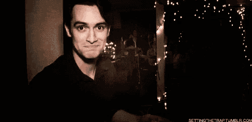 a man is smiling in a dark room with christmas lights behind him .