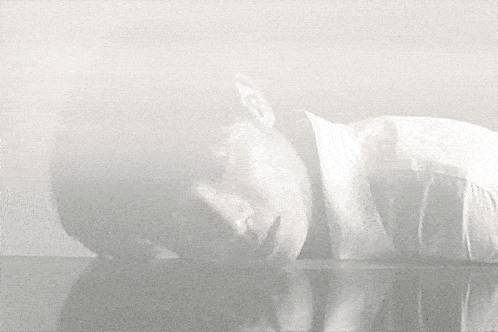 a black and white photo of a man laying on a table with his head on the table .