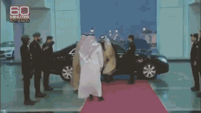 a group of men are standing on a red carpet in front of a car that says 60 minutes on it