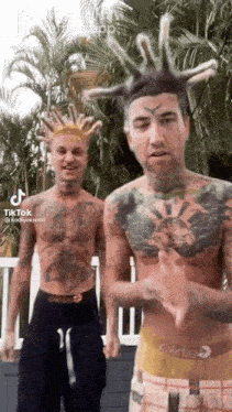 two men with tattoos and dreadlocks are standing next to each other . one of the men has a crown on his head .