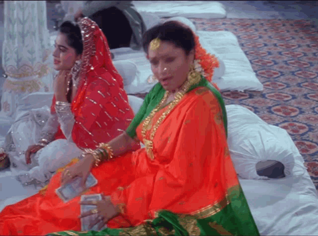two women are sitting on a bed and one is holding money in her hand