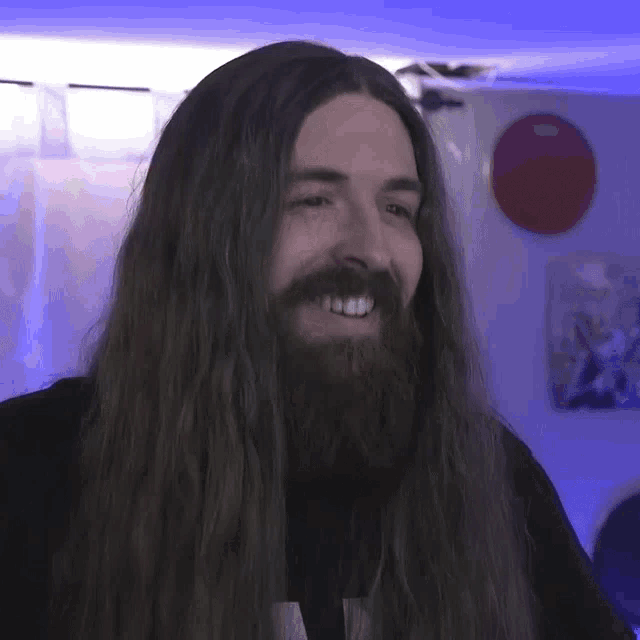 a man with long hair and a beard smiles at the camera